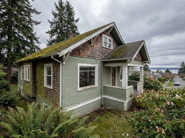 Craftsman house with peeling white trim and faded green siding before repainting